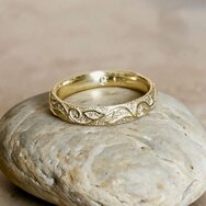 Handcrafted 14k yellow gold wedding ring with floral ornament pattern displayed on a light natural stone