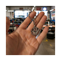 Hand hält runden V8 Schlüsselanhänger aus Messing vor Oldtimer in der Werkstatt.
